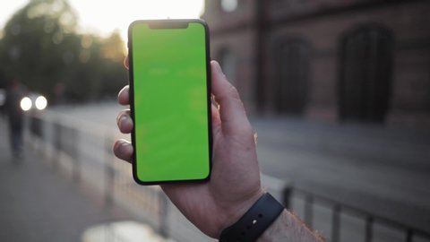 NEW YORK - April 5, 2018: Sunset man hand using iphone with vertical green screen smart mobile view blurred background