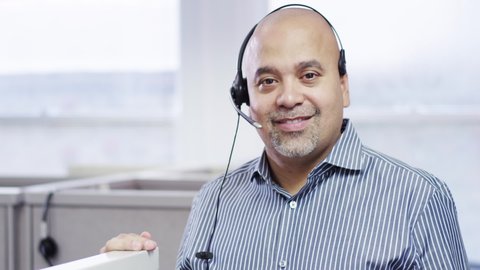 Smiling Hispanic businessman leaning on cubicle posing with headset