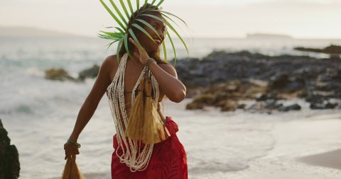 Beautiful polynesian woman performing a Tahitian hula dance on the beach in slow motion at sunset with the ocean moving in the background