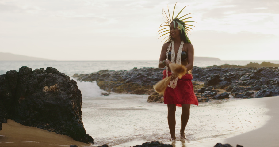 Beautiful polynesian woman performing a Tahitian hula dance on the beach in slow motion at sunset with the ocean moving in the background