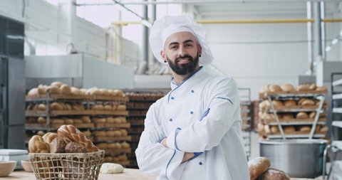 Bakery industry baker chef man with a beard looking straight to the camera smiling large while standing beside his work tablet , then taking details of a bakery basket with organic bread