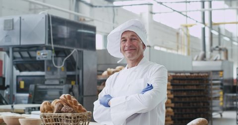 Old man baker portrait looking straight to the camera in a big bakery industry he enjoying the time at his work place