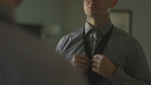 Caucasian man putting tie on at mirror