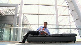 Caucasian businessman laying on bench in atrium reading paperwork