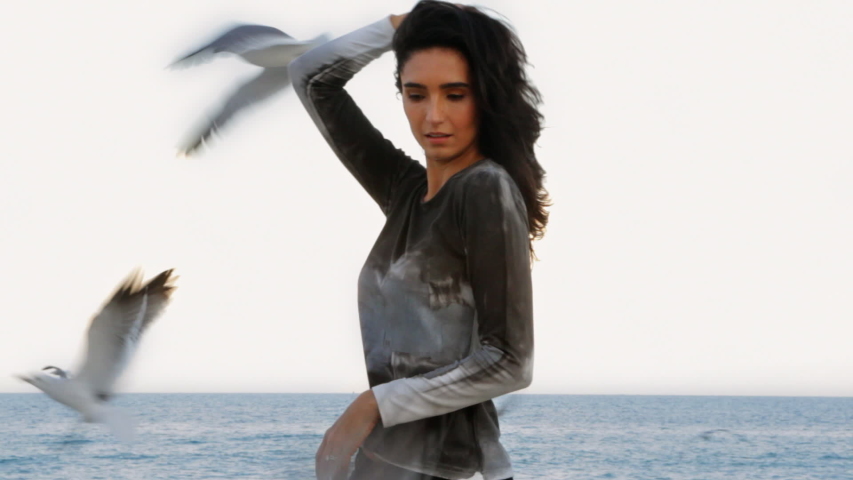 Hispanic woman standing under flock of birds near ocean