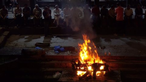 PASHUPATINATH TEMPLE, KATHMANDU, NEPAL - SEPTEMBER 2018: CLOSE UP: Local hindus watch their dead relatives get cremated in an open fire burning inside famous Pashupatinath Temple. Air burial ceremony.