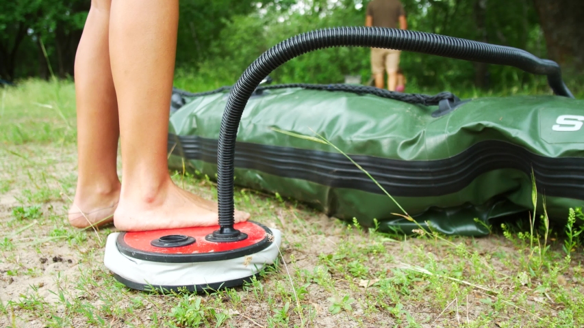 A woman is pumping an inflatable boat with a foot pump.