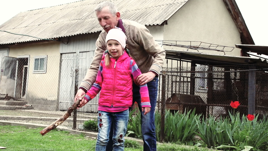 Grandpa has fun with his granddaughter. Grandfather and granddaughter playing a game of skittles outdoor game. Grandfather teaches granddaughter to throw a bat.