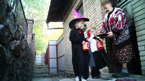 Kids dressed in scary costumes go door-to-door asking strangers for candy. Trick or Treat, kids celebrating halloween.