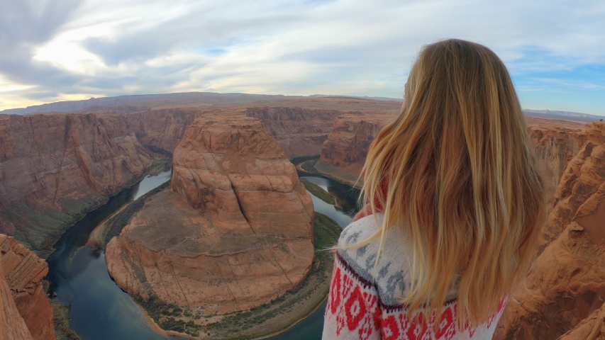 Young woman stands arms wide open above stunning Colorado river. 