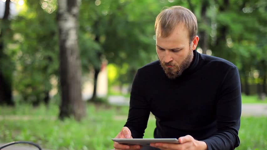 The Young Man With the Tablet Computer on a Bench in the Park