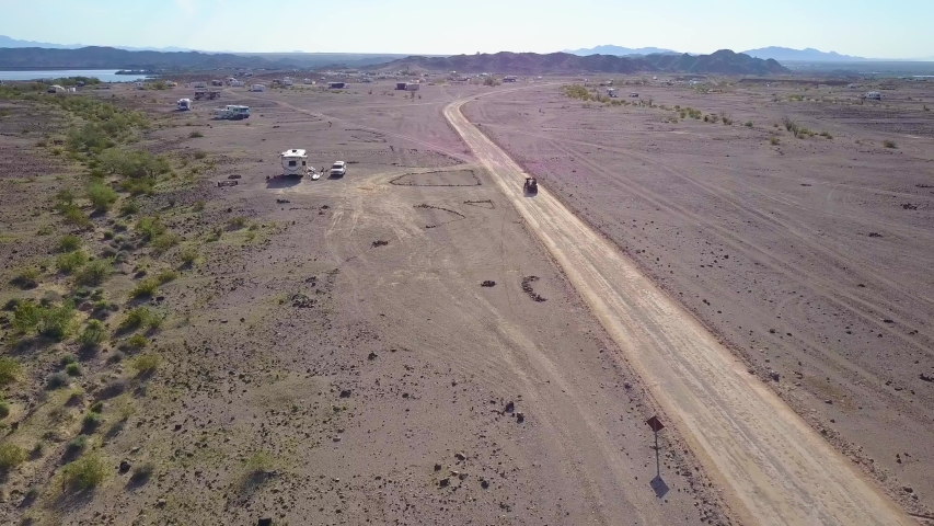 Spectacular aerial drone tracking shot of ATV or All Terrain Vehicle driven next to camper vans in Senator Wash Reservoir overlooking the mountains, located in Colorado River, Southern California
