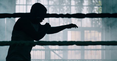 Cinematic slow motion shot of a professional young muscular african man is practicing shadow boxing work out in a ring. 
