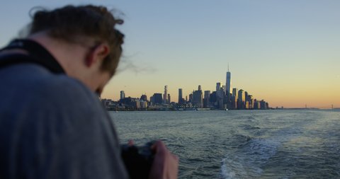 Man Photographing Sunset On Hudson River Moving Away From Incredible New York Sunset And Beautiful Skyscrapers and Iconic Skyline In The Distance .