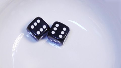 Two black dice bounce and rebound in slow motion on a white background before resting at the numbers six and six, a total of twelve, known as a "Boxcars" or "midnight" in craps.
