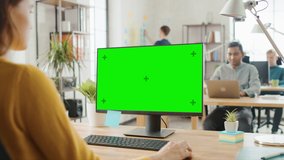 Over the Shoulder: Creative Young Woman Sitting at Her Desk Using Desktop Computer with Mock-up Green Screen. Bright Office where Diverse Team of Young Professionals Work on Computers - Powered by Shutterstock - Get 15% off with code: PIKWIZARD15