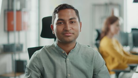 Portrait of Handsome Professional Indian Man Working at His Desk, Using Personal Computer and Smiling at the Camera. Successful Man Working in Bright Diverse Office