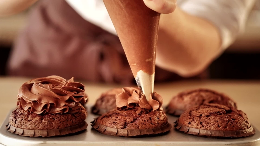 Confectionery decorator. Pastry chef squeezing chocolate frosting on cupcakes from piping bag Royalty-Free Stock Footage #1033127741
