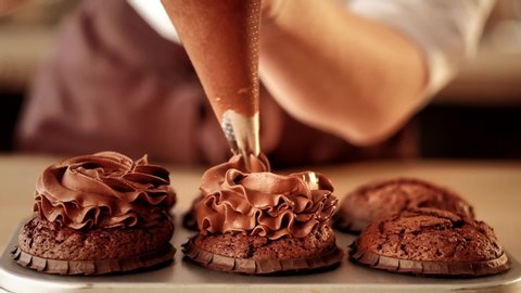 Confectionery decorator. Pastry chef squeezing chocolate frosting on cupcakes from piping bag