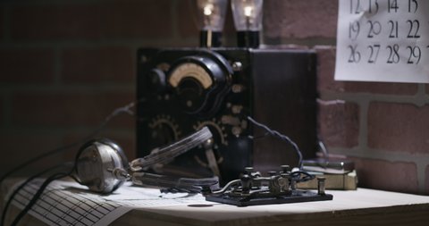 A spy time in the WWII era picks up headphones and commences to transmit messages in Morse Code using a code key.
