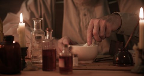 A man skilled in apothecary pours a powdered mixture from a mortar and pestle into a solution then swirls the concoction.