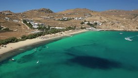 Aerial drone video of famous organised with sun beds and umbrellas beach of  Kalafatis with emerald clear sandy sea shore, Mykonos island, Cyclades, Greece  
