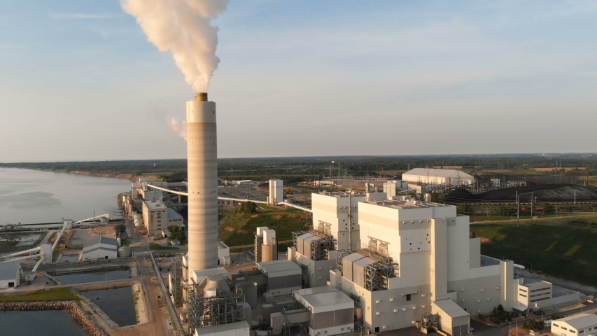 Aerial drone view of a power station on the coast of Lake Michigan at sunrise, Milwaukee, Wisconsin. Beautiful golden sunrise light illuminates the industrial power plant with its smokestacks, cooling towers, and structures right on the lakeshore. Crisp 4K footage captures dramatic aerial perspectives of the facility, steam emissions, the vast expanse of Lake Michigan, and the Milwaukee metropolitan coastline. Highlights the contrast between heavy industry and the natural beauty of the Great Lakes at dawn. Ideal for industrial stock footage, energy sector videos, environmental documentaries, sunrise time-lapse projects, Wisconsin travel, or news content about infrastructure and renewable fossil energy transitions