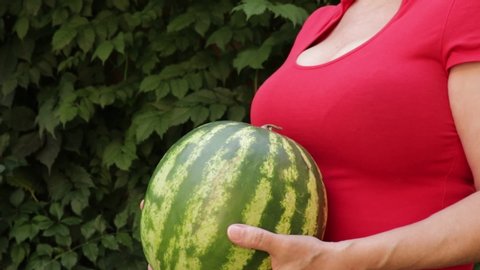 A woman in a red T-shirt with a deep neckline throws a big watermelon up several times and then throws it forward