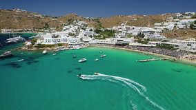 Aerial drone video of famous celebrity sandy beach of Platy Gialos full of luxury yachts and resorts with emerald clear sea, Mykonos, Cyclades, Greece
