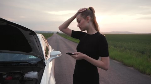 Nervous young woman stand use phone at sunshine looking at engine of breakdown car at the field alone automobile girl help lost road trouble upset side transportation travel close up slow motion