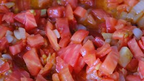 White onion chopped into small pieces stewed with red fresh tomatoes with olive oil on a non-stick griddle, video clip close-up shooting