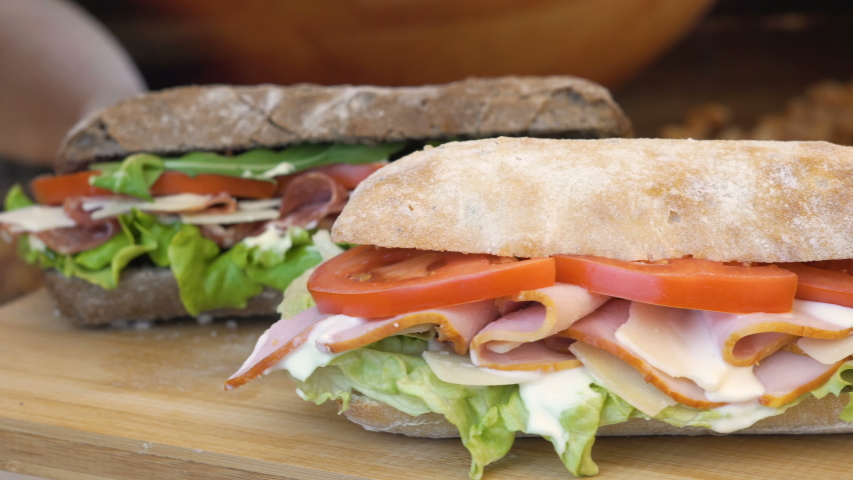 Static shot of a turkey bread roll and a balkan sandwich, with sallad, rucola, tomatoes and cucumber slices, moving around on a wooden table. Royalty-Free Stock Footage #1033159166