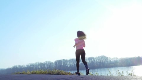 sportive girl jogging along the river bank during sunrise or sunset. healthy lifestyle concept of athletic woman goes in for sports. slow motion