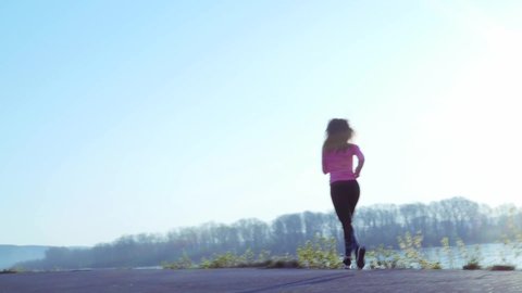 sportive girl jogging along the river bank during sunrise or sunset. healthy lifestyle concept of athletic woman goes in for sports. slow motion