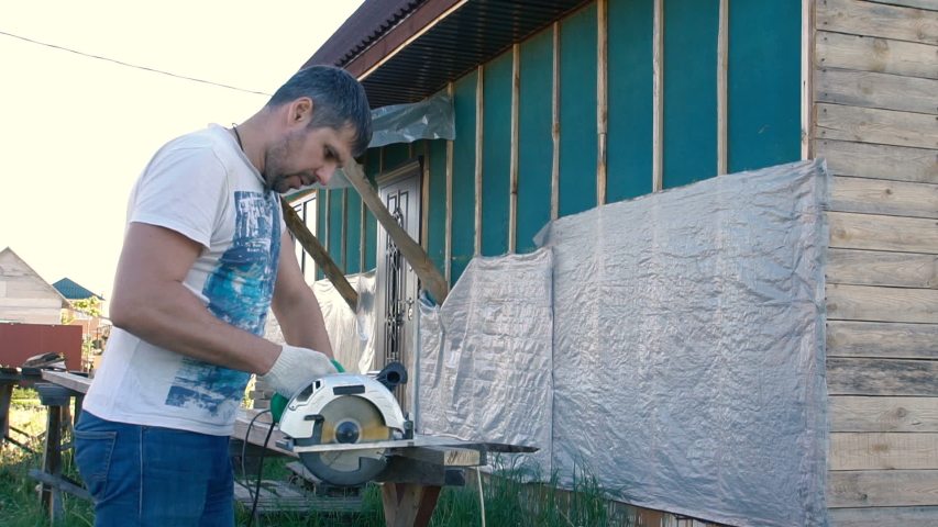 A man works with an electric saw. Wearing a white T-shirt and jeans. Home construction. Father of the family. Working. Master. Electric tool.