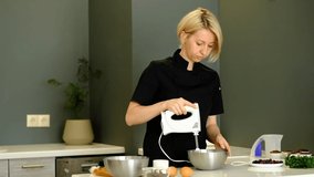 Professional Baker Whipped chocolate cream for cake or pastries in a bowl. small business. young woman cook in a black suit in the modern kitchen