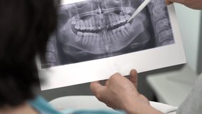 Dentist is showing to his patient a result of her orthopantomogram in a dental clinic. Closeup video recording from behind.