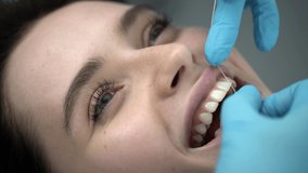 Gorgeous girl in a dental clinic. Dentist in blue latex gloves is flossing her teeth with a help of a dental floss. Closeup video recording.