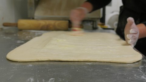 woman adding layer of butter to large cinnamon roll dough. Woman spreads melted butter to dough.