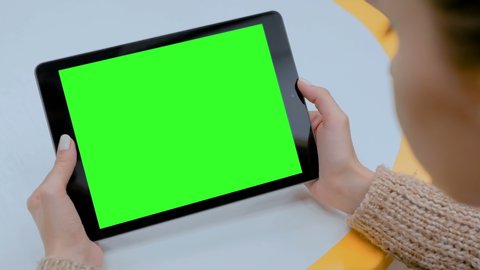Woman looking at black digital tablet computer device with empty green screen on table at home. Technology, chroma key, template, mock up and entertainment concept