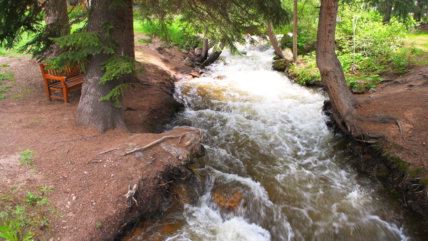 Mountain stream of Gore creek river with flowing water and bench by shore in Vail, Colorado resort town city