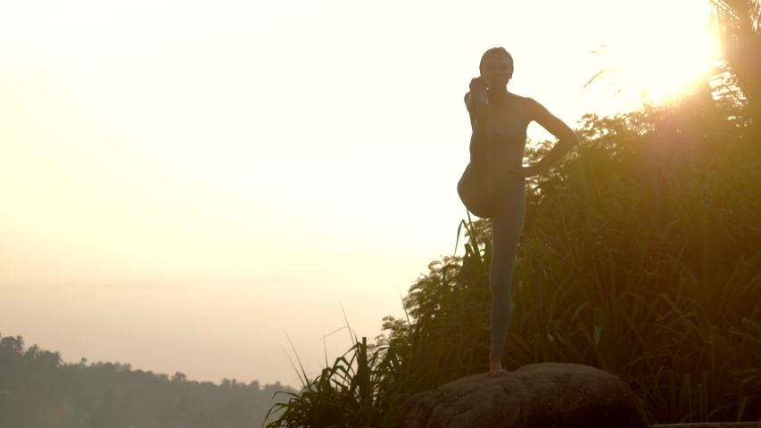 Athletic girl shows utthita hastapadangusth asana standing on big rock at sunrise time low angle shot slow motion. Concept fitness yoga wellness lifestyle | Shutterstock HD Video #1033195781