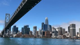 4K HD video passing under West end of the Bay Bridge heading into Downtown San Francisco, viewed from a boat in the bay rocking from the current on a sunny day blue sky. Iconic city establishing shot