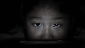 Night shoot: Little child playing smartphone lying on bed, light and the blue light has a negative effect on the child's eyes. Health care concept
