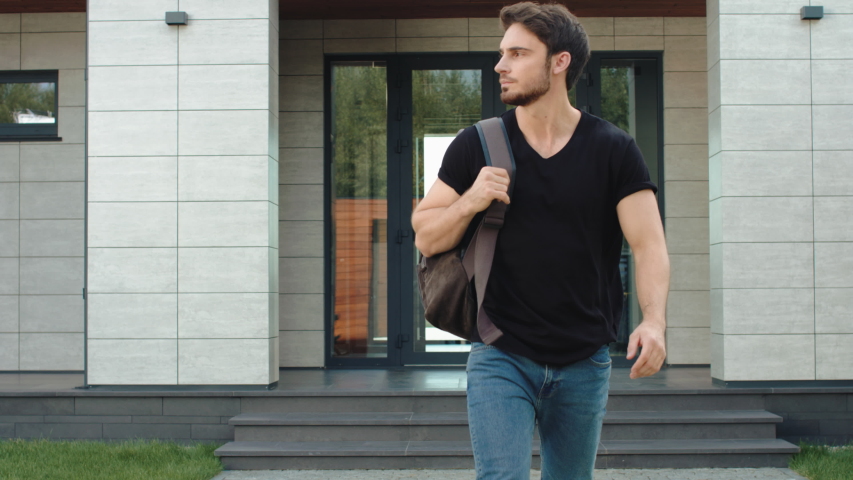 Casual man going down stairs from modern building with backpack. Portrait of male employee leaving office building. Caucasian programmer going outside luxury house. Handsome man leaving apartments