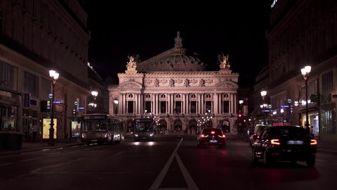 PARIS, FRANCE - June 17 2019: Locked down real time establishing shot of Opera Garnier at night. Night time people walking around and traffic on the street, June 17, 2019 in Paris, France.