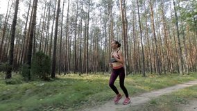 Happy young woman is jogging in a forest among trees. Tracking shot with stabilized camera