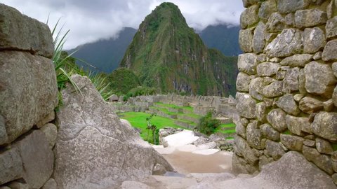 Machu Picchu Landscape reveal. Slow track past ancient stone wall to reveal misty Machu Picchu - Panning shot of the magnificent ancient citadel high in the Andes mountain range.