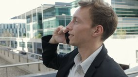 Side view of happy young Caucasian man talking on phone outside business office, smiling. Lifestyle, communication concept