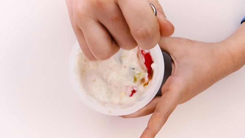 yogurt and fruits. Female hand scoops up yogurt with fruits from a jar with a spoon. Top view.